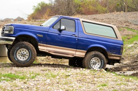 1996 Ford Bronco - This blue 1996 Ford Bronco navigates a muddy off-road trail with its tan top and trim visible.