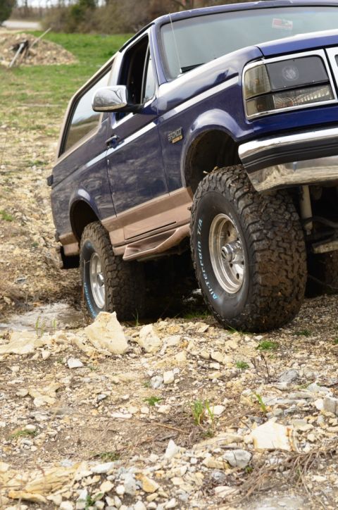 1996 Ford Bronco - This blue Ford Bronco is navigating a rough, rocky path with its tires gripping the uneven ground.