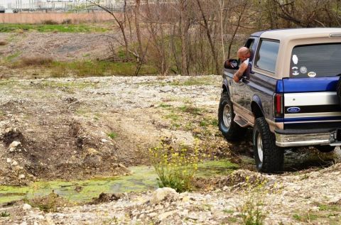 1996 Ford Bronco - A blue and tan 1996 Ford Bronco navigates a muddy, off-road terrain.