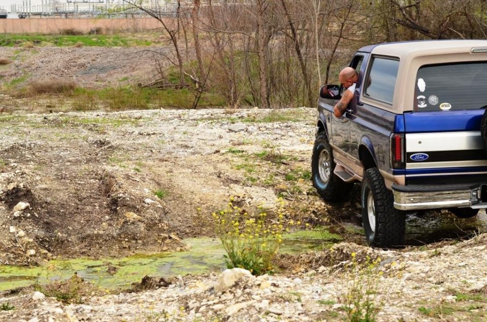 Blue and tan 1996 Ford Bronco driving off-road, rear view