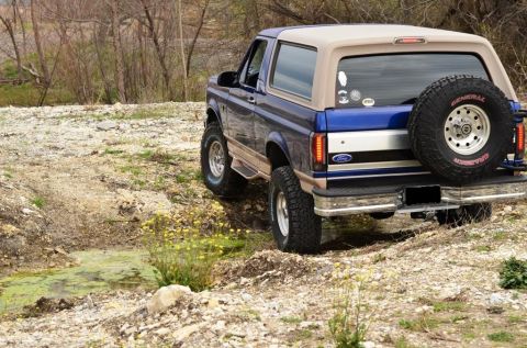 1996 Ford Bronco - This 1996 Ford Bronco is shown from the rear, navigating an off-road trail with a spare tire mounted externally.