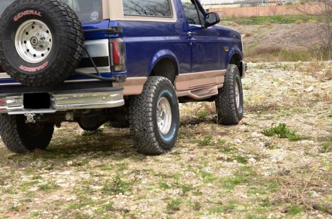1996 Ford Bronco - This Ford Bronco is parked on a dirt lot with sparse vegetation.
