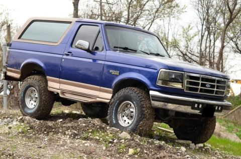 1996 Ford Bronco - A blue 1996 Ford Bronco with tan trim is shown on an off-road trail.