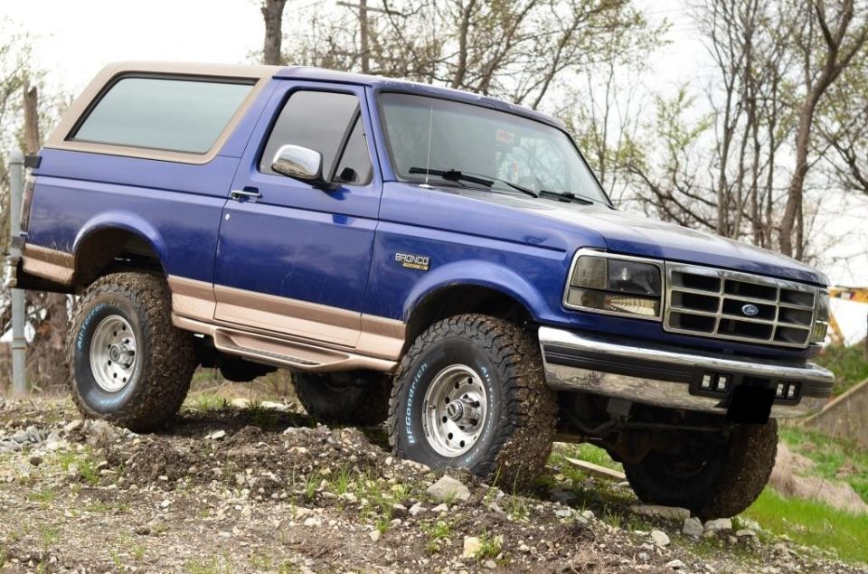 Blue 1996 Ford Bronco with tan trim on a dirt incline, front 3/4 view