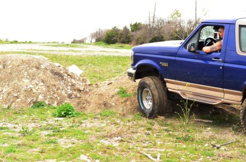 1996 Ford Bronco - A blue 1996 Ford Bronco navigates an off-road course, climbing a dirt embankment.