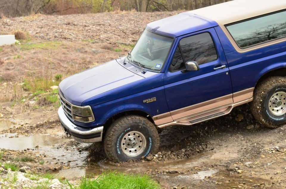 Blue 1996 Ford Bronco navigating a muddy trail, tires deep in the muck