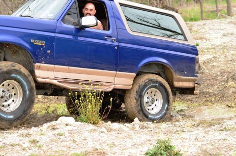 1996 Ford Bronco - A man drives a blue Ford Bronco through a muddy, off-road trail.