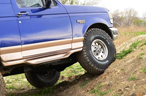 1996 Ford Bronco - A blue 1996 Ford Bronco navigates an off-road incline, its tires gripping the dirt.