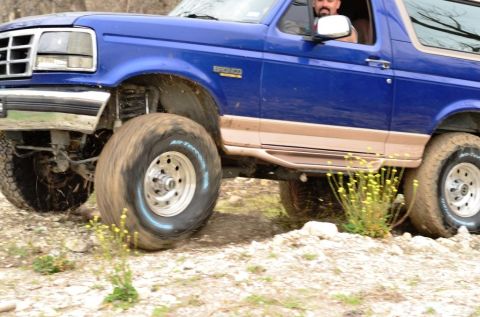 1996 Ford Bronco - This 1996 Ford Bronco is captured in action, navigating a rough, off-road terrain with its suspension clearly engaged.