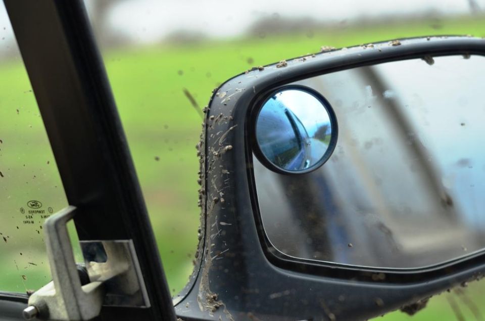 Side mirror and window of a dirty vehicle, showing reflection of road ahead