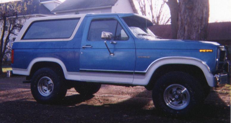 Side view of a blue and white Ford Bronco SUV with alloy wheels, parked outdoors near a tree
