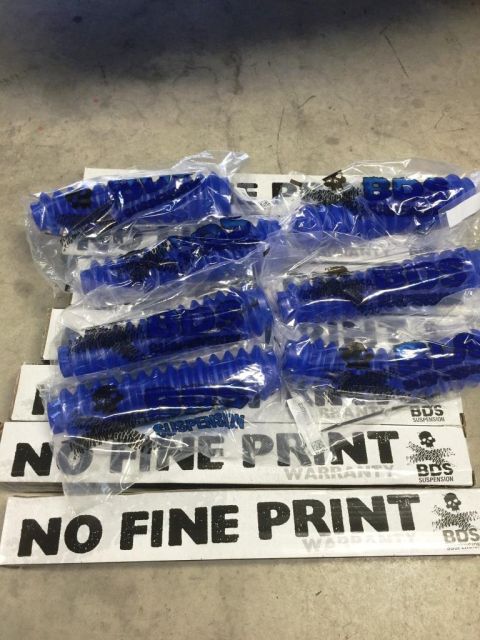 1996 Ford Bronco - Several blue shock dust boots are packaged and stacked on top of boxes that say "NO FINE PRINT".