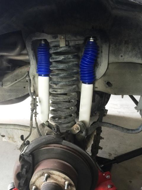 1996 Ford Bronco - Close-up view of the front suspension system, blue and white shock absorbers and coil springs.