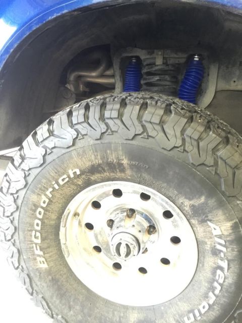 1996 Ford Bronco - Close-up of a vehicle's rear wheel, suspension, and exhaust system, blue shocks.