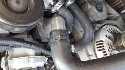 1995 Ford Mustang - A close-up view of the engine bay of a 1995 Ford Mustang, focusing on the thermostat housing and various hoses connected to it. The alterna…