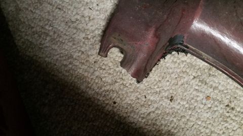 1995 Ford Mustang - A close-up view shows a damaged section of a dark red car part resting on a textured carpet. The edge of the part is broken and frayed, wit…