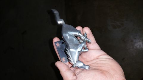 1995 Ford Mustang - A person holds a chrome Mustang horse emblem with a black mounting bracket attached. The emblem is angled to show its dynamic pose and meta…