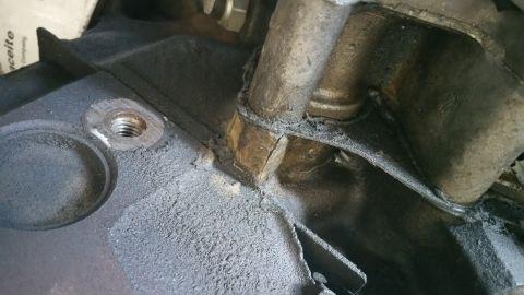1995 Ford Mustang - A close-up view of a heavily soiled engine block with a metal pipe attached. The engine block has a threaded hole visible on the left side.