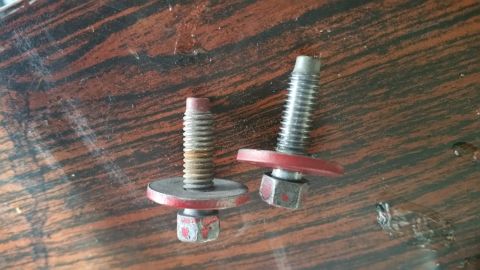 1995 Ford Mustang - Two bolts with red washers and nuts are shown on a wooden surface. One bolt appears slightly rusted.