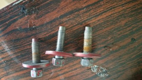 1995 Ford Mustang - Three bolts with red washers and nuts are shown on a wooden surface. The bolts appear to be used and show signs of rust and wear.