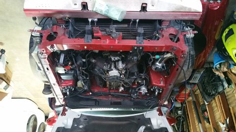 1995 Ford Mustang - Overhead view of a red Ford Mustang engine bay with the front fascia removed, revealing the engine, radiator, and various hoses and wiring.