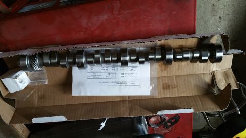 1995 Ford Mustang - A camshaft is shown laid out in a cardboard box, with a white paper document detailing its specifications underneath. The camshaft is metal…