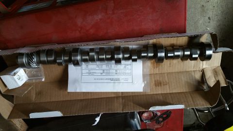 1995 Ford Mustang - A camshaft with a gear on one end is laid out in a cardboard box. A white document with specifications is placed beneath the camshaft.