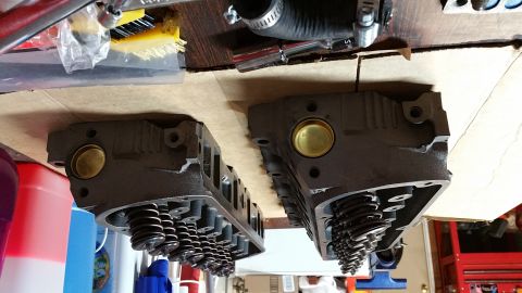 1995 Ford Mustang - Two cast iron cylinder heads with visible valve springs and brass plugs are laid out on a cardboard surface. Tools and various containers a…