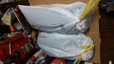 1995 Ford Mustang - Two white plastic bags are tied with yellow plastic ties and sit on top of a cardboard box. The bags contain dark, lumpy contents. Tools an…