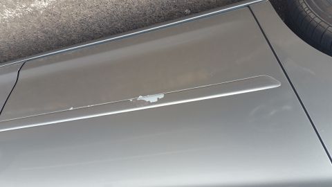 1995 Ford Mustang - The side of a silver vehicle shows peeling paint on a body trim piece. The vehicle is parked on asphalt.