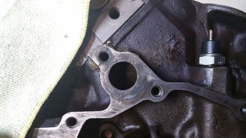 1995 Ford Mustang - A close-up view of an engine block with a gasket and a bolt with a rubber grommet and nut attached. A light-colored cloth is visible in the…