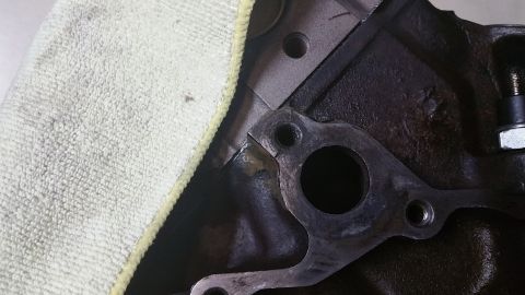 1995 Ford Mustang - A close-up view of a dark-colored engine block with a metal gasket attached. A white microfiber cloth is partially visible in the upper lef…