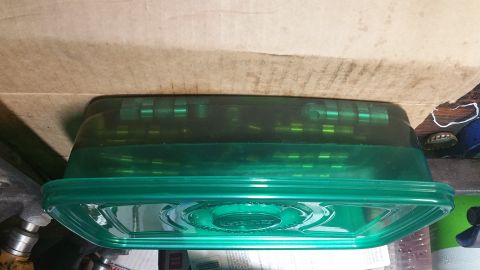 1995 Ford Mustang - A green plastic food container with a ribbed lid sits on a piece of cardboard. The container has a textured pattern on the lid.