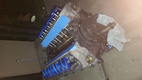 1995 Ford Mustang - A disassembled V8 engine block with blue valve covers and silver rocker arms is laid out on a concrete surface. Blue painter's tape covers…