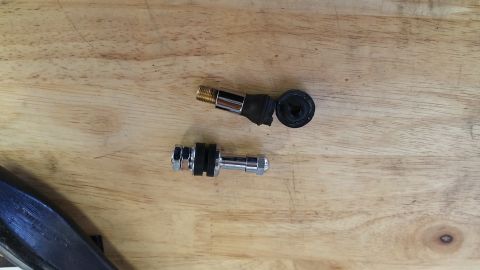 1995 Ford Mustang - Two tire valve stems are shown disassembled on a wooden surface. One stem has a brass threaded end and a black rubber base, while the other…