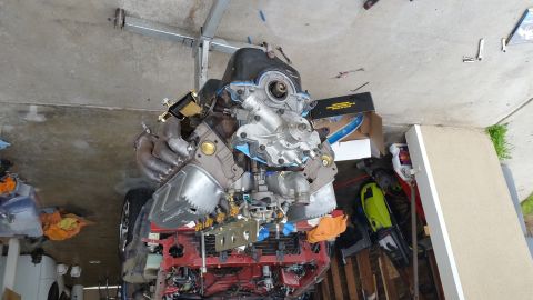 1995 Ford Mustang - A V8 engine with exhaust manifolds and a water pump is mounted on an engine stand in a garage. Tools and other automotive parts are scatter…