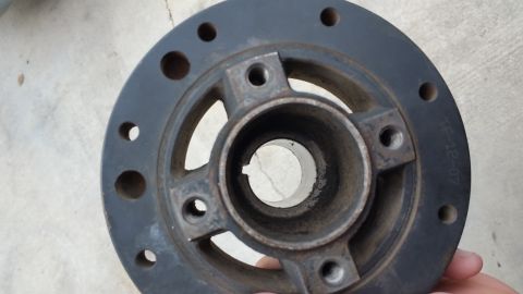 1995 Ford Mustang - A close-up view of a dark gray metal pulley or hub with a central bore featuring a keyway. The part has several bolt holes around its perim…