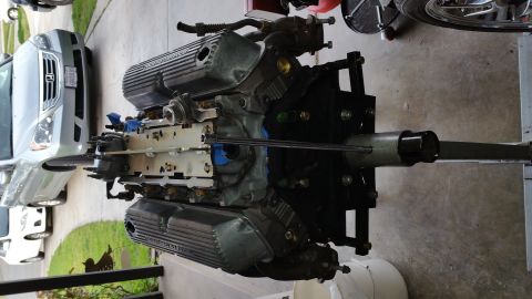 1995 Ford Mustang - A V8 engine is mounted on an engine stand, with valve covers that read "POWERED BY FORD". A silver SUV is parked in the background.