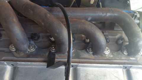 1995 Ford Mustang - Close-up view of a V8 engine's exhaust headers and spark plugs, bolted to the engine block with shiny hardware. A black cable runs vertical…