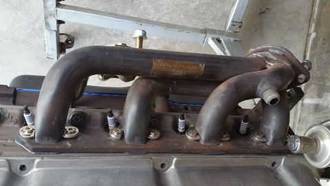 1995 Ford Mustang - A close-up view shows a custom exhaust manifold attached to a Ford engine block. Spark plugs are visible, along with a metal plate on the m…