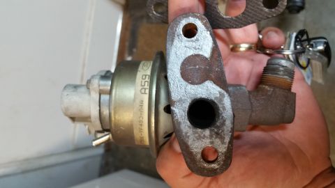 1995 Ford Mustang - A hand holds a turbocharger wastegate actuator with a metal gasket and keys attached to a ring. The actuator has a label with the text "A59…