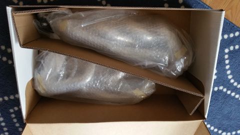 1995 Ford Mustang - Two car parts, wrapped in plastic and bubble wrap, are packed inside an open cardboard box. The box is placed on a blue and white patterned…