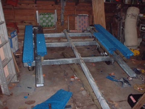 1996 Ford Taurus - The metal frame of a boat trailer, equipped with blue carpeted bunks, sits on the floor of a cluttered garage.