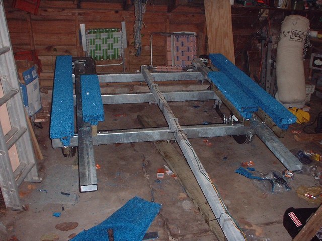 Boat trailer frame with blue carpeted bunks inside a garage