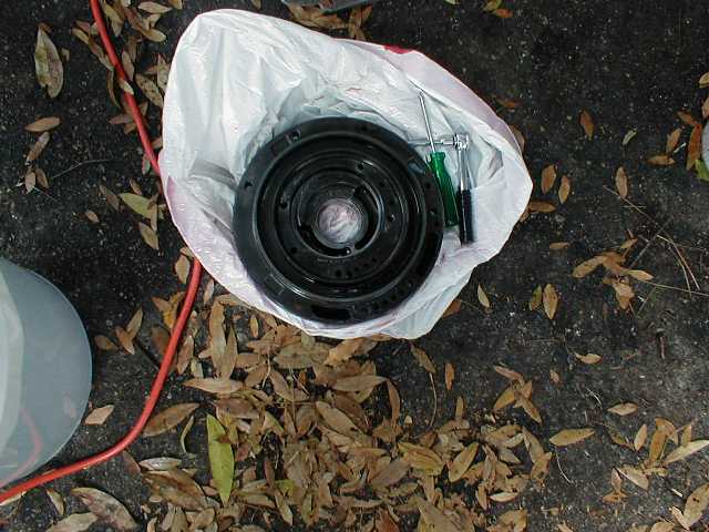Black brake or hub drum sitting in a white plastic bag on leaf-strewn pavement, red air hose nearby