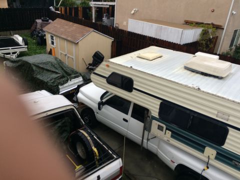 1987 Suzuki Samurai - Multiple vehicles are parked in a yard, including a pickup truck with a camper shell.