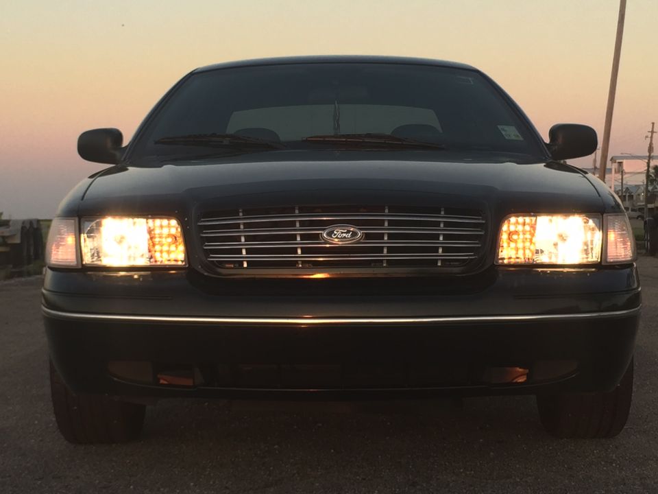 Black Ford Crown Victoria sedan, front view, headlights on, dusk lighting