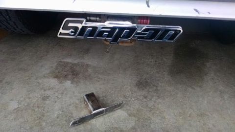 1994 Ford Bronco - A chrome Snap-on logo is attached to the rear bumper of a vehicle, with a trailer hitch receiver and a metal accessory lying on the concret…