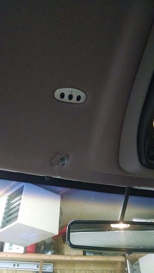 1994 Ford Bronco - The interior of a vehicle shows a garage door opener unit with three buttons mounted on the headliner. A rearview mirror and a white vent a…