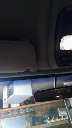 1994 Ford Bronco - Interior view of a vehicle showing the overhead console with a light, a sun visor, and a rearview mirror reflecting a garage scene with she…